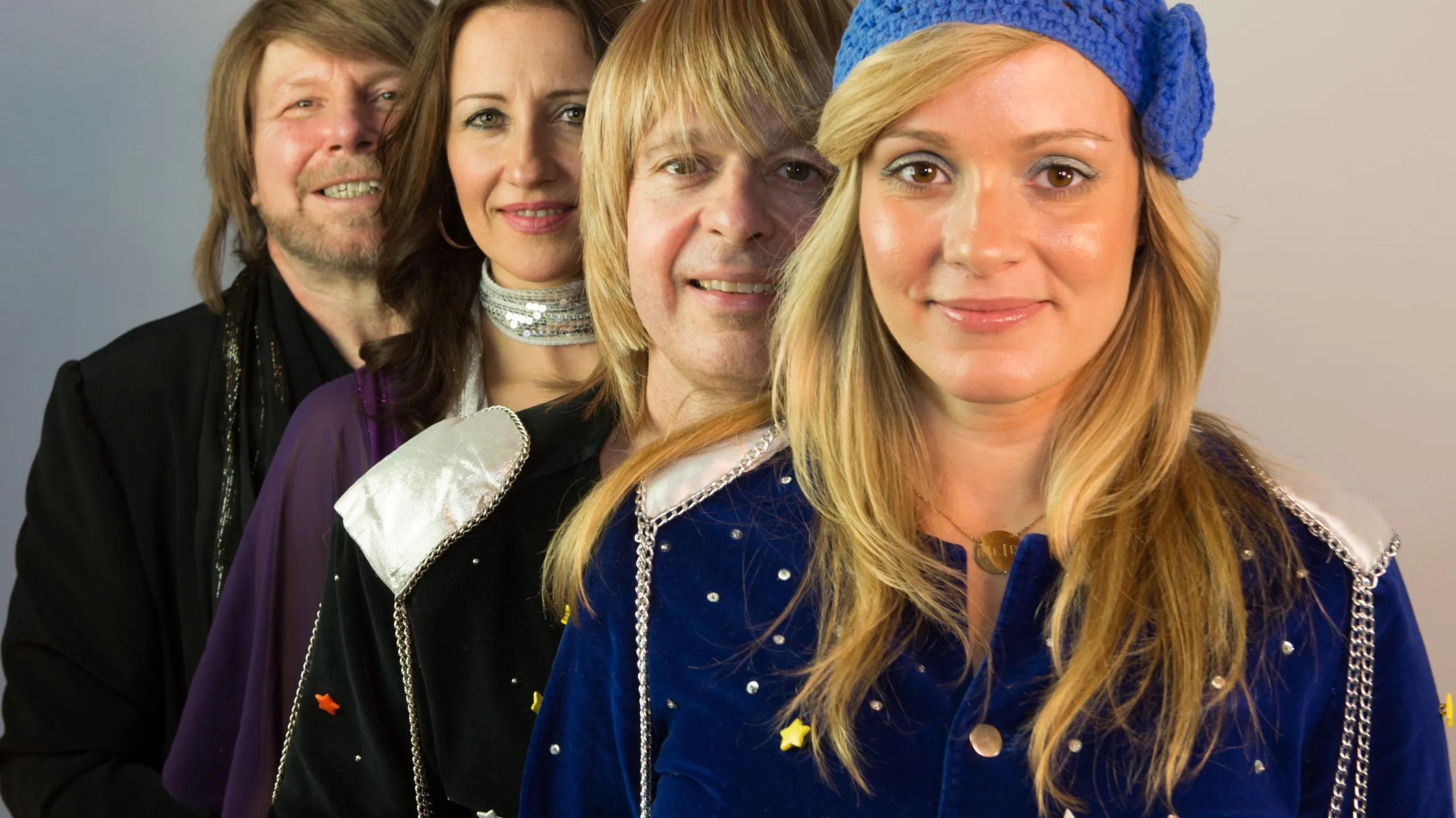 Two men and two women pose together in seventies-period clothing. 
