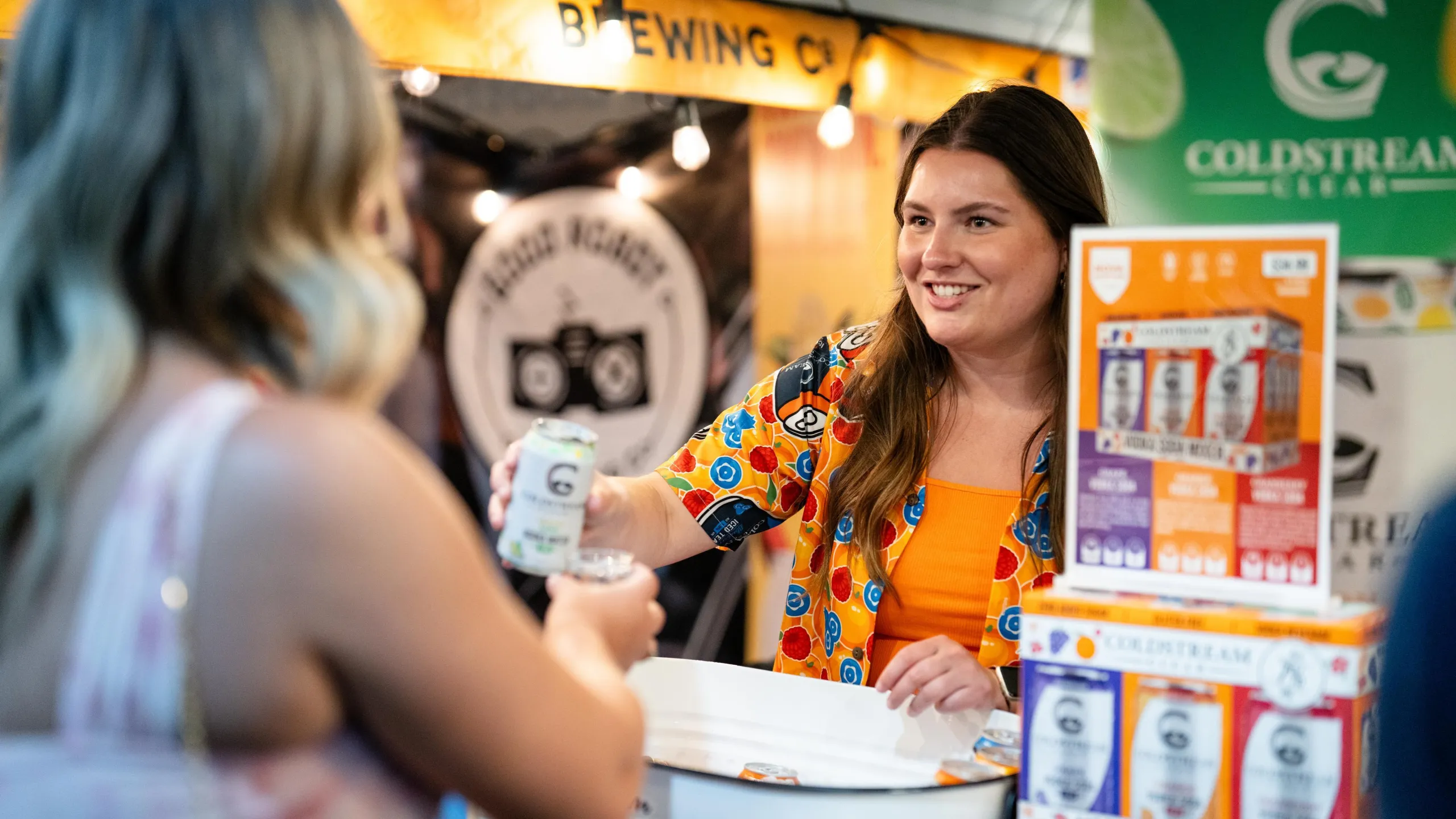 A woman at a trade show booth pouring a sample drink for a customer