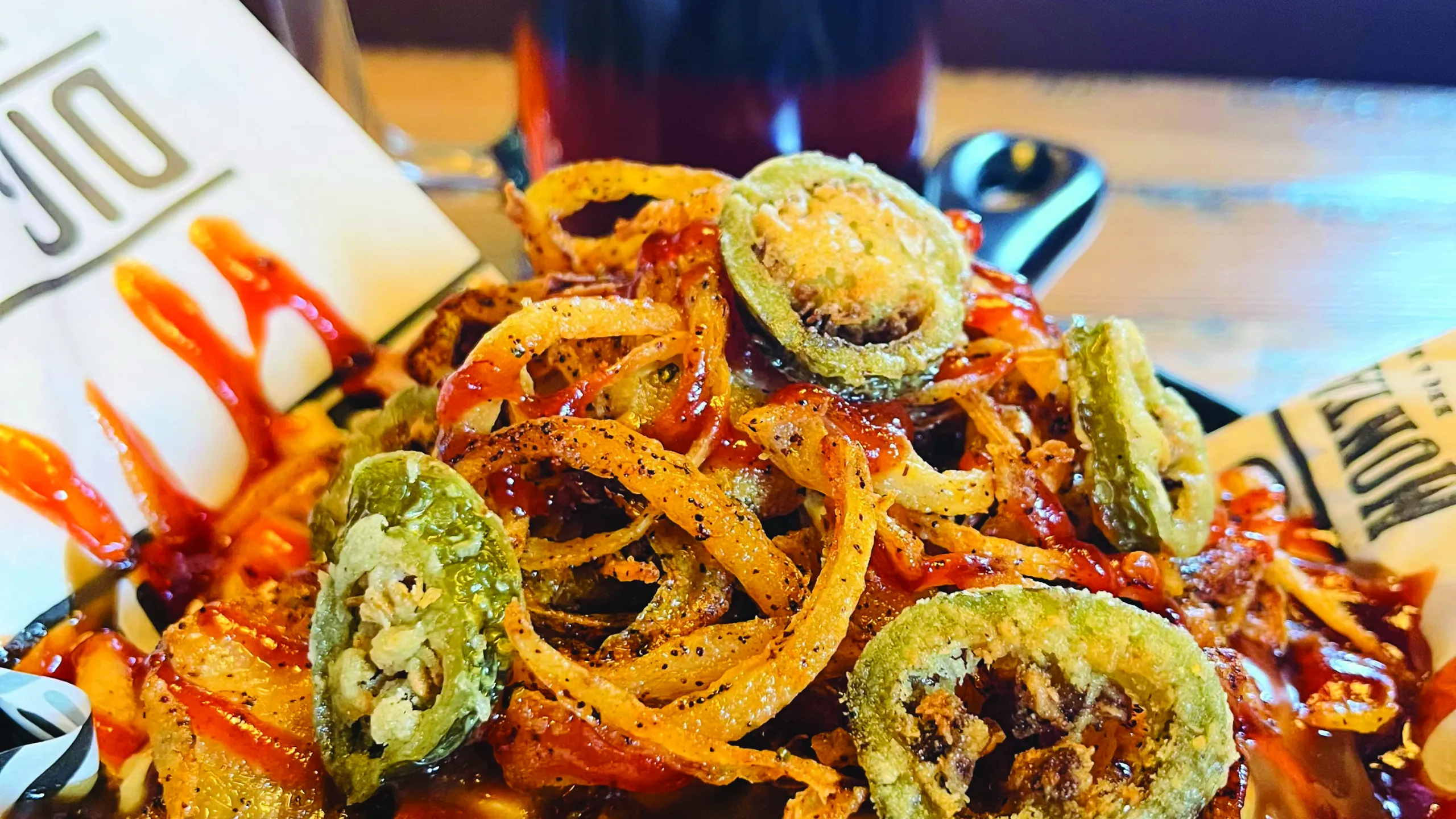 A plate of poutine heaped with fried jalapenos and onion rings.