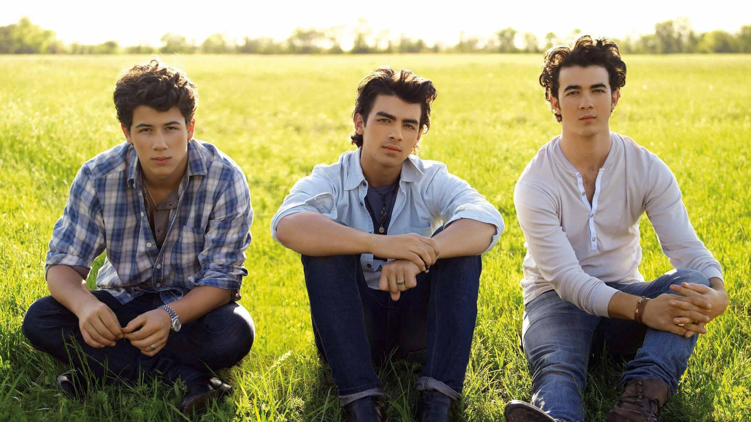 Jonas Brothers sitting on grass in a field