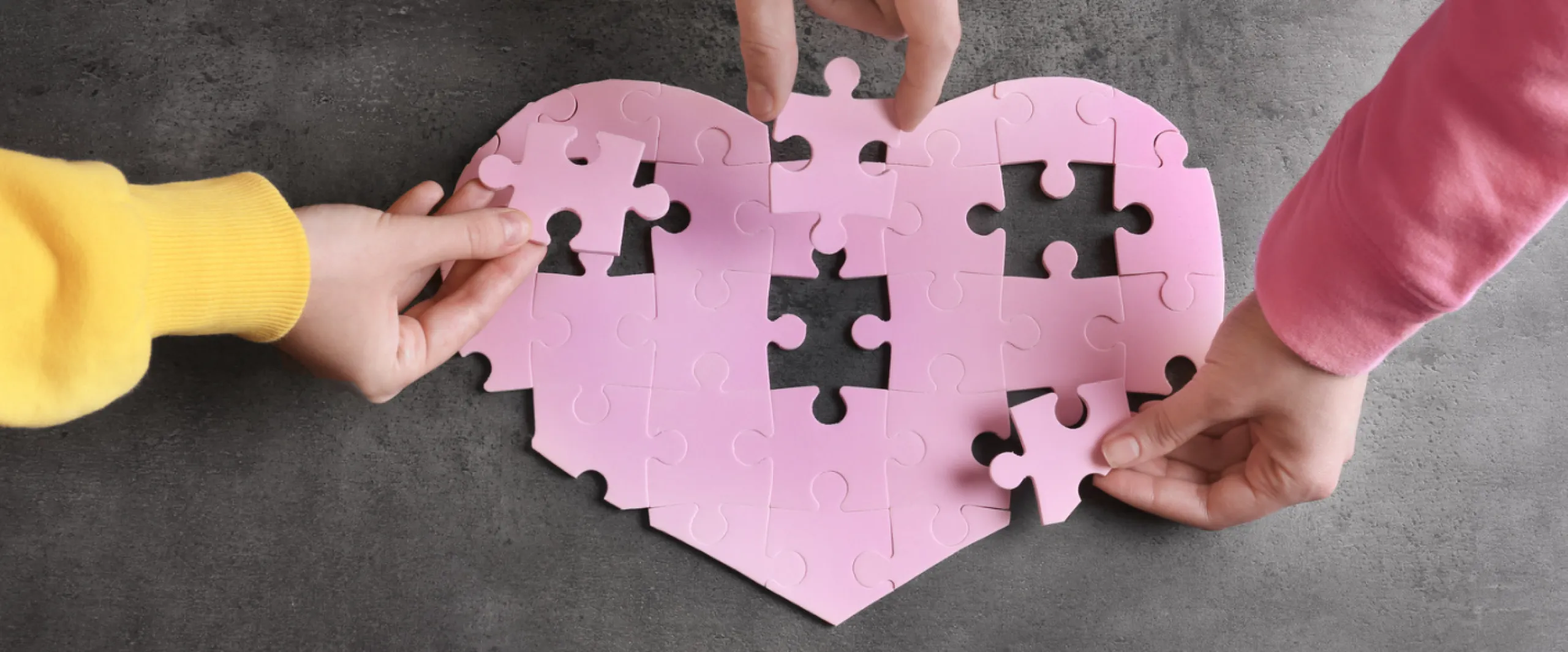Hands assembling puzzle pieces in shape of heart